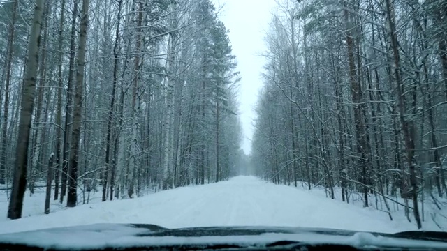 一辆汽车在大雪中沿着一条覆盖着积雪的森林道路行驶。视频素材