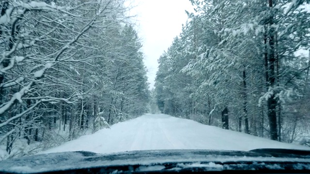 一辆汽车在大雪中沿着一条覆盖着积雪的森林道路行驶。视频素材