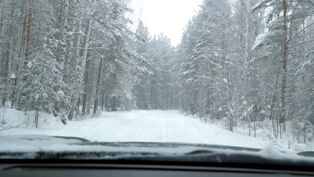 一辆汽车在大雪中沿着一条覆盖着积雪的森林道路行驶。视频素材