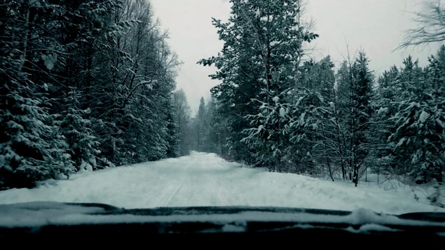 一辆汽车在大雪中沿着一条覆盖着积雪的森林道路行驶。视频素材