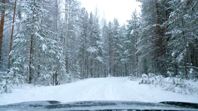 一辆汽车在大雪中沿着一条覆盖着积雪的森林道路行驶。视频素材