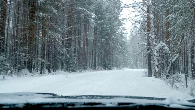 一辆汽车在大雪中沿着一条覆盖着积雪的森林道路行驶。视频素材