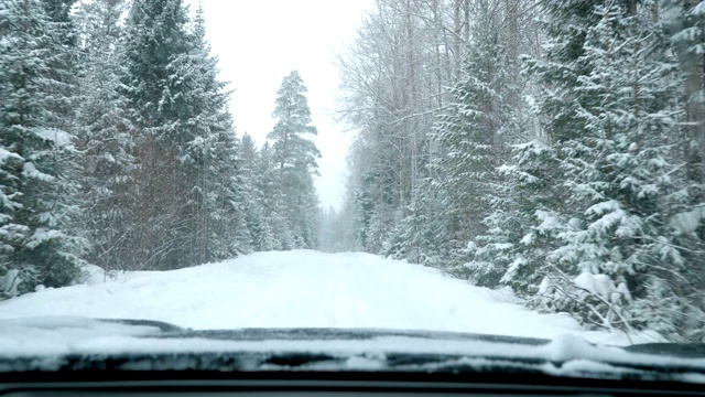 一辆汽车在大雪中沿着一条覆盖着积雪的森林道路行驶。视频素材