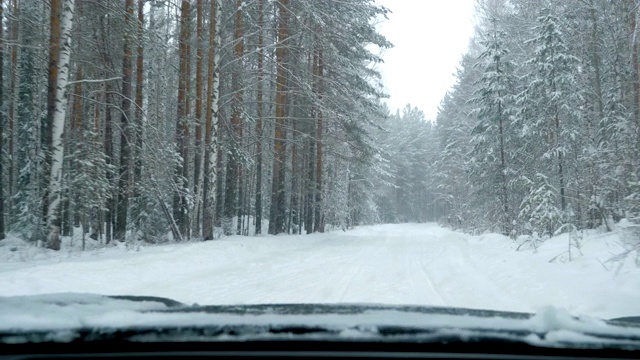 一辆汽车在大雪中沿着一条覆盖着积雪的森林道路行驶。视频素材