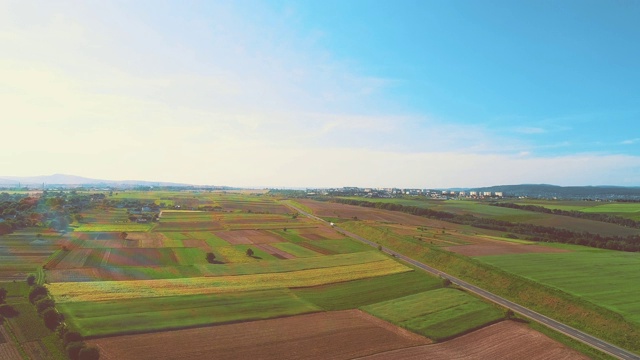 空中飞过田野间的道路，画面一开始就有彩虹砖，蓝色的天空充满了光和温暖。4 k。视频素材