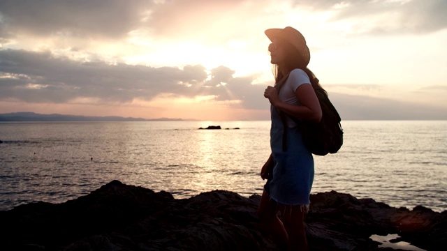 剪影的女性游客与背包和帽子欣赏惊人的海景日落视频素材