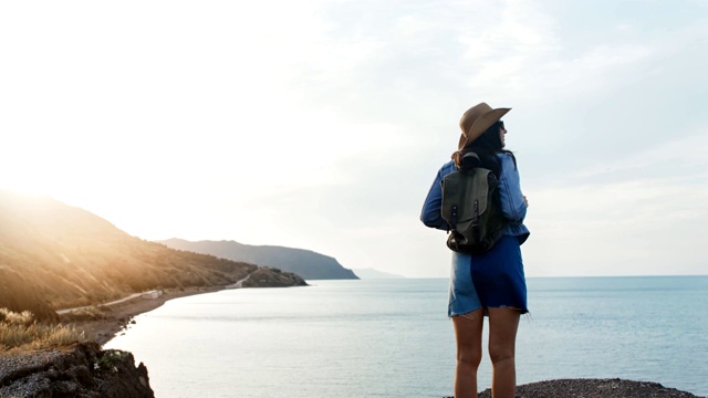 后视图活跃的背包女接近大海，从山上欣赏令人惊叹的海景视频素材