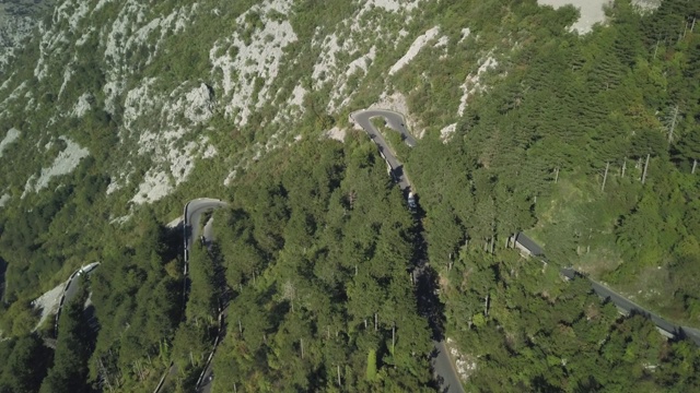 鸟瞰图山形蜿蜒的道路与卡车和汽车。股票。道路交通蜿蜒在高山狭窄的角落，汽车变成绿色的森林视频素材