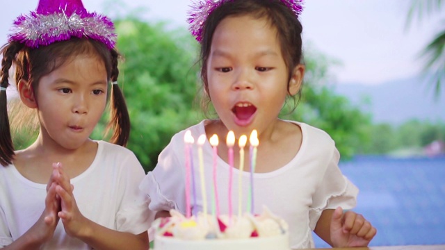 亚洲女孩和她的妹妹唱歌和吹蜡烛在生日蛋糕视频素材