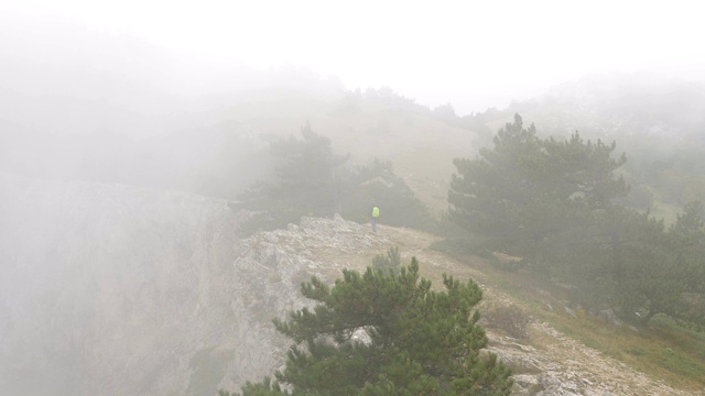 一个年轻人背着背包走在布满云的岩石山脊上。视频素材