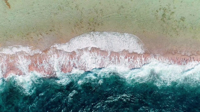 海浪撞击着热带海滩上的珊瑚礁。一半是蓝色的海浪，一半是太平洋的海滩和珊瑚。海浪很大。旅行热带概念-鸟瞰无人机- 4K视频素材