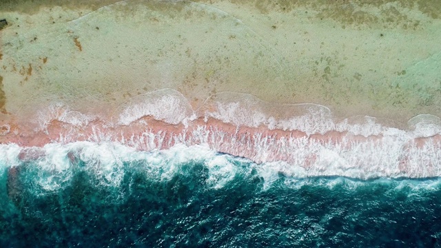 海浪撞击着热带海滩上的珊瑚礁。一半是蓝色的海浪，一半是太平洋的海滩和珊瑚。海浪很大。旅行热带概念-鸟瞰无人机- 4K视频素材