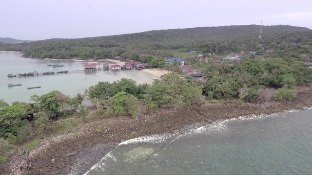 从空中拍下被海浪淹没的海滩上的石头和鹅卵石。小渔村为背景视频素材