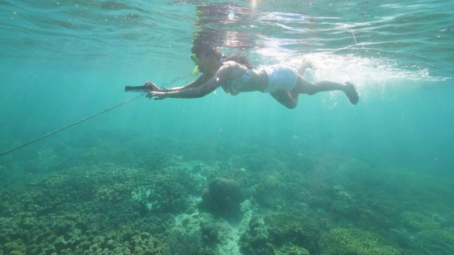 年轻女子在透明的海水中戴着通气管面罩和移动相机浮潜。水下风景女孩游泳在潜水面罩和管珊瑚礁在蓝色的海洋。视频素材