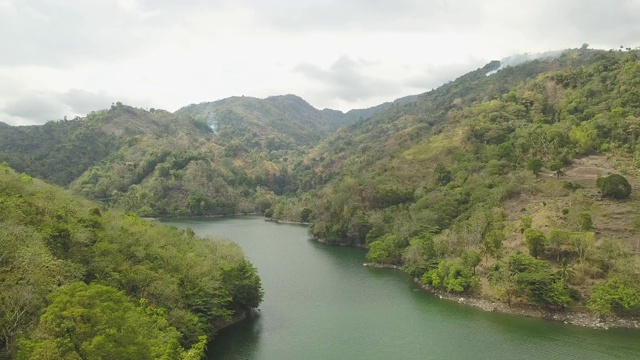 无人机拍摄的热带湖泊和绿色高地景观。空中景观绿色的山丘覆盖热带植物和河流在多云的天空背景。视频素材