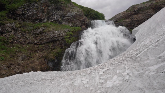 夏季山地景观:高山瀑布落入雪原视频素材