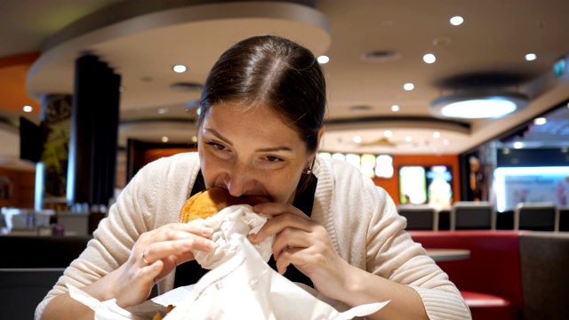 年轻的黑发女子正在美食广场的快餐店里吃汉堡。视频素材