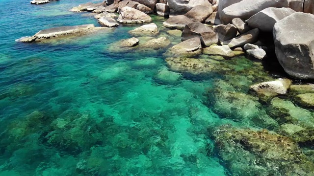 石头附近有平静的海水。在泰国阳光明媚的日子里，宁静的蓝色海水和灰色的巨石是潜水的完美场所。自然背景纹理。视频素材