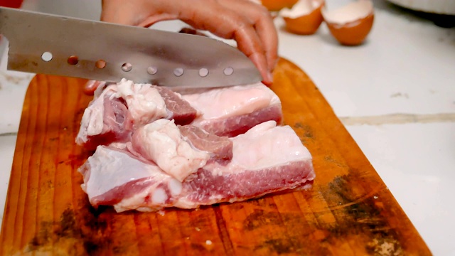 在厨房的砧板上，妇女们用刀将猪肉切成小块视频素材