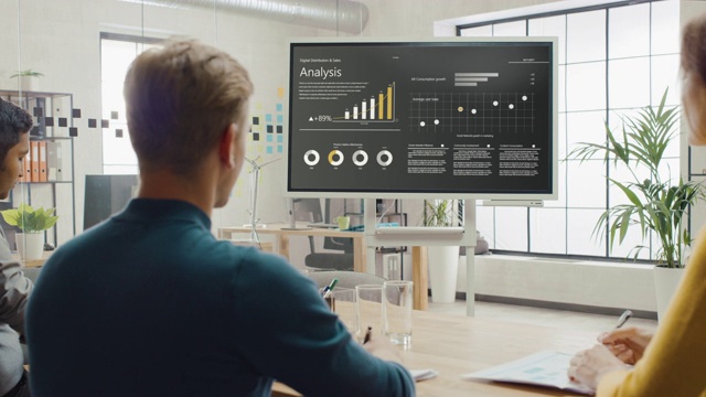 分析团队，经济学家和年轻的商人举行会议演示使用显示数字互动白板增长分析，图表，统计和数据。人们在创意办公室工作视频素材