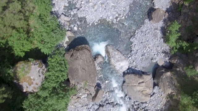 无人机俯瞰快速流动的高山冰川河在一个郁郁葱葱的绿色高山森林山谷。视频素材