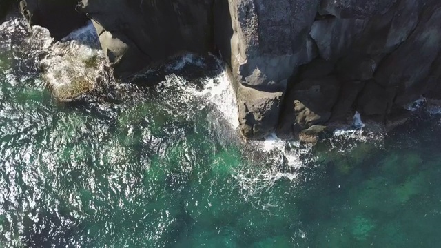 海浪溅到岩石悬崖无人机视图。透明的海浪打破岩石悬崖与浪花和泡沫从无人机鸟瞰图。视频素材