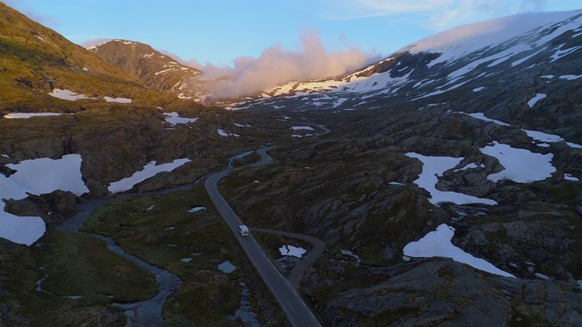 航拍:露营车在挪威达尔斯尼巴山高原的岩石和积雪中行驶视频素材