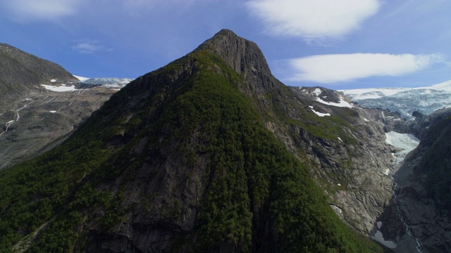 航拍:岩石山脉上的苔藓，与冰川和天空相映衬的雪花——挪威布里克斯达尔冰川视频素材