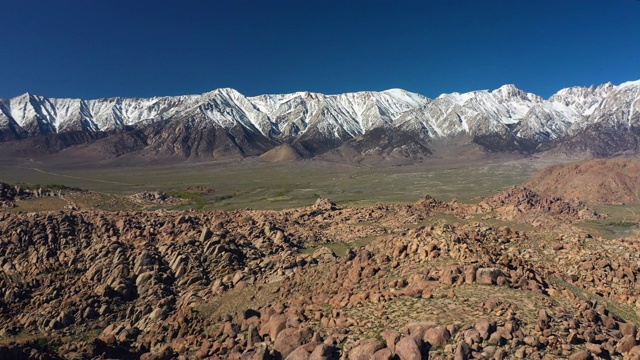 空中的潘:岩石山，绿色的滚动平原，和雪峰在阳光日-阿拉巴马山，加利福尼亚视频素材