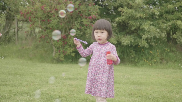 蹒跚学步的小女孩在自家花园里玩肥皂泡视频素材