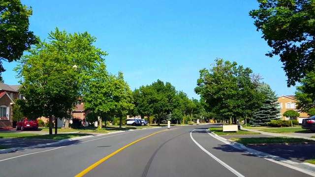 夏季，在绿树成荫的住宅城市道路上驾驶接近停车标志。司机视角:沿着美丽的阳光郊区街道慢过停车标志。视频素材