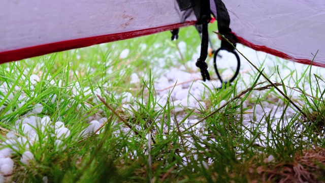 夏天的中午，雷特扎特山的布库拉湖，冰雹落在帐篷上。从帐篷里面看，绿色的草地上有很多冰雹。山区恶劣的天气条件。视频下载