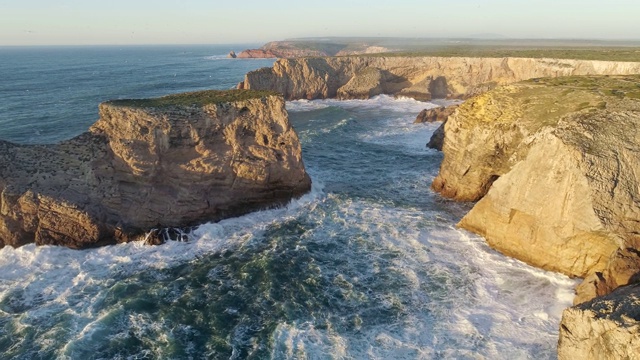 日落时的岩石和海洋，在葡萄牙的圣文森特角(Cabo de Sao Vicente)，欧洲大陆的最西南点。泛着泡沫的绿松石般的海浪翻滚着冲击着海岸。空中,4 k视频素材