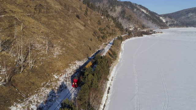 空中:一列红色的旅客列车停在山间和结冰的贝加尔湖之间的铁轨上视频素材