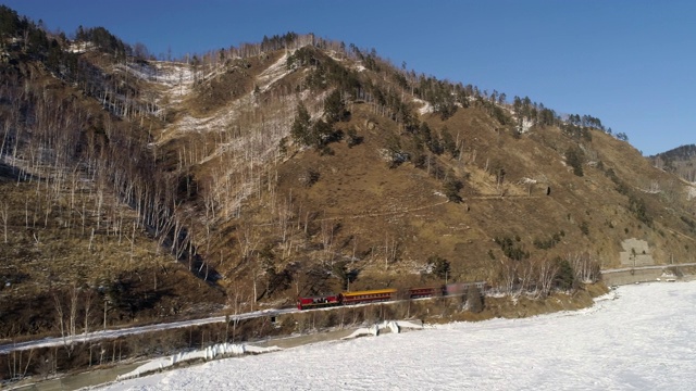 空中:在晴朗的天空下，旅客列车沿着雄伟的山脉和冰冻的贝加尔湖旅行视频素材