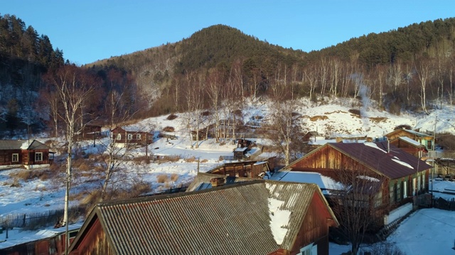 空中:俄罗斯贝加尔湖，冬季，无人驾驶飞机接近树木山上陆地上的房屋视频素材