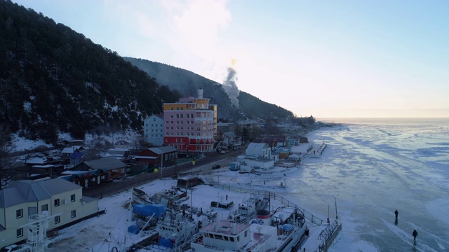 航拍:冰封的贝加尔湖边的房屋和天空下的山脉视频素材