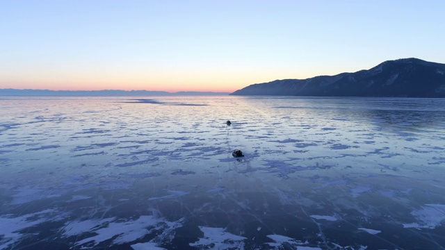 航拍:在夕阳下，水陆两栖车辆在结冰的贝加尔湖上行驶，湖面上是橙色和蓝色的天空视频素材