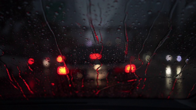 抽象模糊的雨，当汽车在道路中间的夜晚汽车尾灯反射雨滴在汽车的镜子视频素材