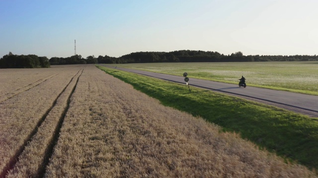 直路在农业边。一名男子骑着摩托车在夕阳中经过。鸟瞰图。4 k视频素材