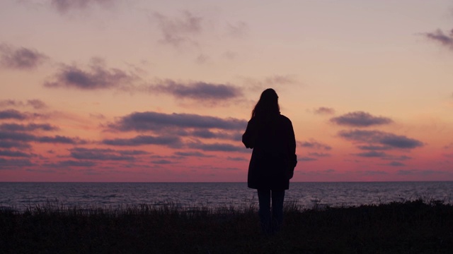 夕阳西下，女人独自站在海边视频素材