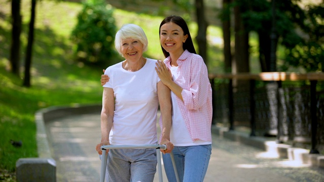 年轻女性拥抱老年妇女与步行架户外，康复视频素材