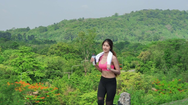 美丽的亚洲女人在自然，树木和阳光在晚上的道路上慢跑或跑步的慢动作视频剪辑。健康运动的概念。视频素材