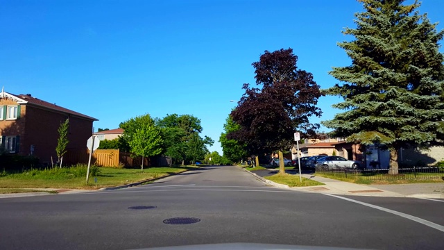 夏季驾驶在绿树成荫的住宅区城市道路拐弯处。司机视角:沿着美丽的阳光郊区街道转弯。视频素材