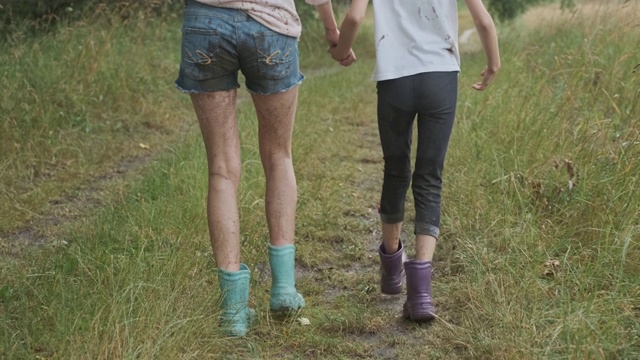 两个快乐的女孩姐妹在雨后挽着脏衣服散步，孩子们谈笑风生，乡间小路上夏日的大自然背景回眸视频素材