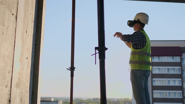 工程师建造者在日落时分站在建筑的屋顶上，用VR眼镜想象建筑平面图，并使用未来的界面移动他的手。视频素材