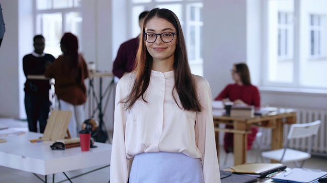 中等肖像美丽的年轻聪明的黑发商务女人在眼镜看在时髦的阁楼办公室的相机。视频素材