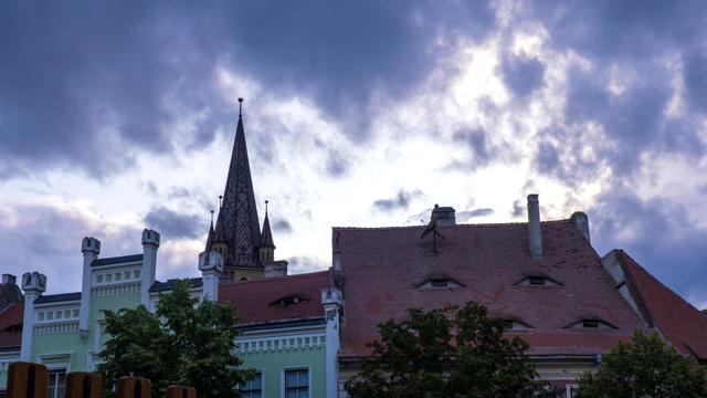 时间:罗马尼亚西比乌(Hermannstadt)小广场上戏剧性的乌云和日落天空，后面是教堂塔楼，前面是传统房屋。向上倾斜，ProRes 422, 4K。视频下载