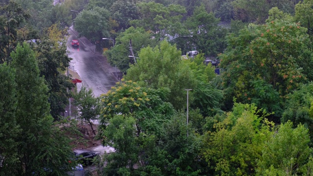 鸟瞰雨点落在城市住宅区，有很多绿树，而街道上有几辆车经过。城市的雨季。视频下载