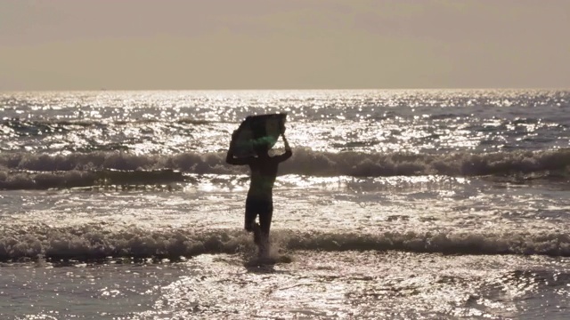 小男孩在海里奔跑，带着滑板冲向海浪视频素材